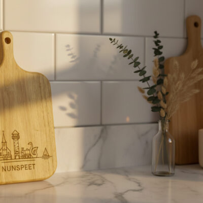 Skyline Serveerplank Nunspeet – Massief Eiken met Lasergravure Eikenhouten serveerplank met gegraveerde skyline , liggend op een houten tafel met kaas, noten en een glas rode wijn.