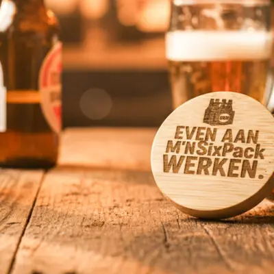 Ronde houten bieropener met gegraveerde tekst , gemaakt van bamboe met metalen onderzijde. Ambachtelijk gegraveerd door De Meesterbrander.
