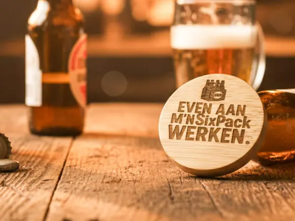 Ronde houten bieropener met gegraveerde tekst , gemaakt van bamboe met metalen onderzijde. Ambachtelijk gegraveerd door De Meesterbrander.