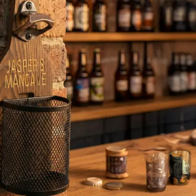 Houten Wandbieropener met Dopjesmandje Afneembaar metalen dopjesmandje gevuld met bierdopjes bij houten wandbieropener