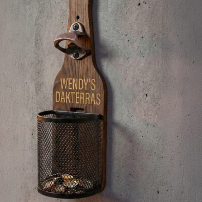 Afneembaar metalen dopjesmandje gevuld met bierdopjes bij houten wandbieropener