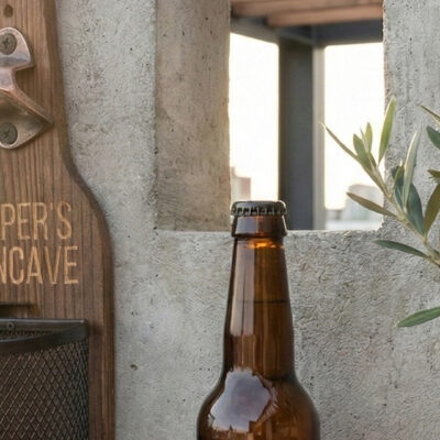 Afneembaar metalen dopjesmandje gevuld met bierdopjes bij houten wandbieropener