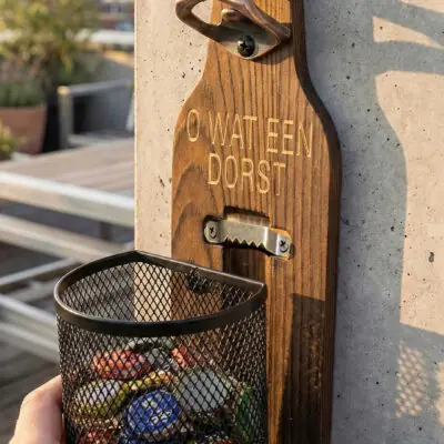 Houten Wandbieropener met Dopjesmandje Afneembaar metalen dopjesmandje gevuld met bierdopjes bij houten wandbieropener