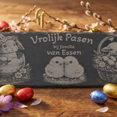 Rechthoekige leisteen met gravure van konijn, kuikens en lammetje omringd door kleurrijke paaseitjes op een houten tafel.